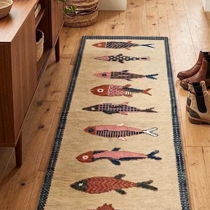 May include: A rectangular beige rug with a navy blue border features a repeating pattern of stylized fish in various colors, including red, pink, and black. The rug is placed on a wooden floor, adding a touch of coastal decor.