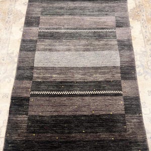 May include: A rectangular area rug with a striped pattern in shades of gray, black, and brown. The rug features a white zigzag design and small flecks of color. The rug is a neutral color and would complement any room.