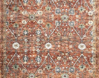 May include: A rectangular area rug featuring a deep terracotta red background with a repeating lattice pattern of white, blue, and sage green floral motifs. The design includes intricate geometric lines and a decorative border in muted earth tones.