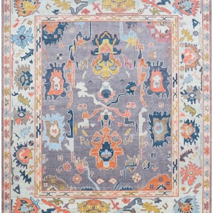 May include: A rectangular area rug with a central design in shades of gray, orange, blue, and yellow. The rug features an intricate pattern with floral and geometric motifs. The border is a lighter color with similar patterns, creating a cohesive design.