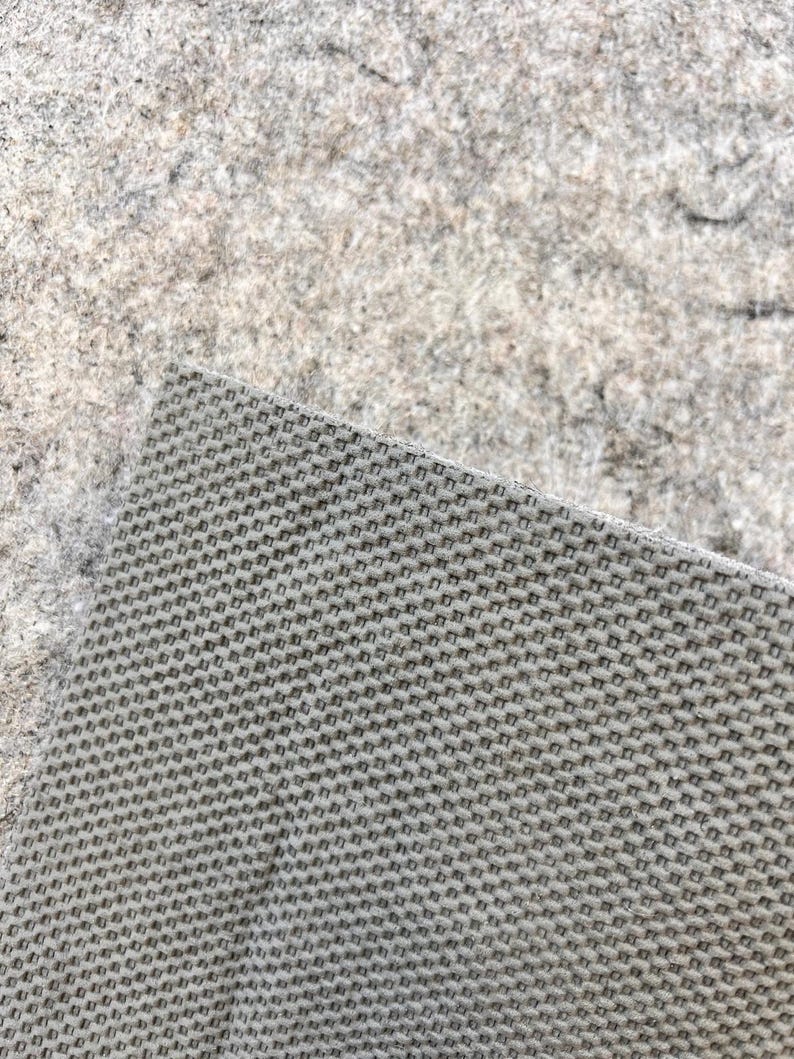 May include: Close-up of a gray woven fabric with a fine, even texture. The fabric has a slightly rough surface.