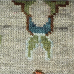 May include: Close-up of a textured rug with a repeating floral pattern. The rug features a light gray background with accents of teal, pink, green, and brown. The design is symmetrical, with the floral elements evenly spaced across the surface.