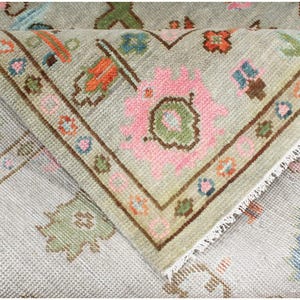 A close-up of a light green rug with a pink and white floral pattern. The rug has a fringe border and is folded over on itself. The rug is made of a soft, woven material.