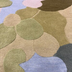 May include: A colorful, abstract rug featuring a pattern of organic shapes in various shades. The rug incorporates hues of green, brown, blue, and pink, creating a soft, textured surface. The design is reminiscent of a landscape or a map.