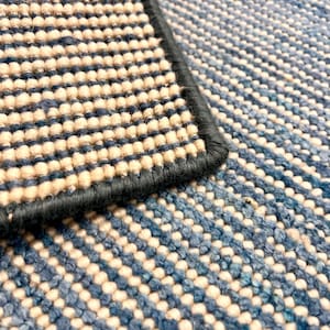 May include: Close-up of a textured rug with a blue and cream pattern. The rug has a dark blue border and a woven design. The color palette includes shades of blue and cream, creating a visually appealing textile.