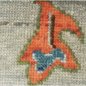 May include: Close-up of a textured rug with a repeating pattern. The design features a light gray background with orange, green, and blue floral motifs. The rug's texture is visible, with a dense, looped pile.