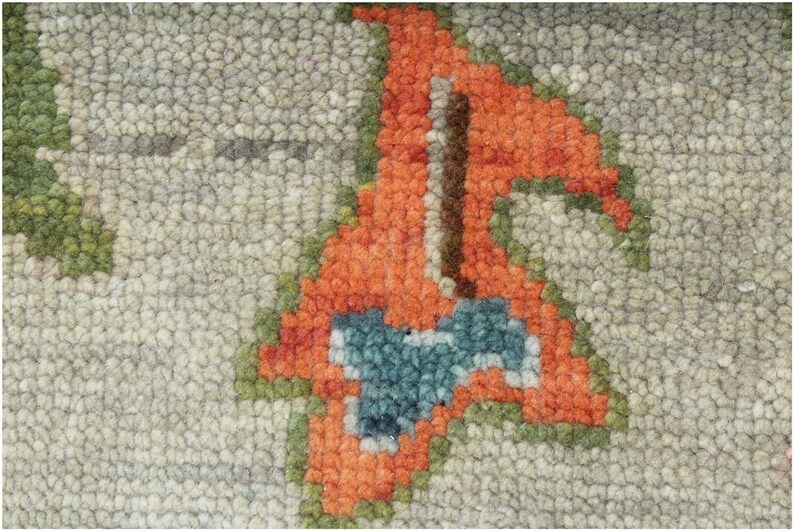 May include: Close-up of a textured rug with a repeating pattern. The design features a light gray background with orange, green, and blue floral motifs. The rug's texture is visible, with a dense, looped pile.