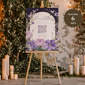 以下が含まれることがあります： QRコード付きの紫色の花柄の結婚式席次表。QRコードには「席を探すためにスキャンしてください」と表示されています。サインには「Take a Seat」、「The Smiths」、「May 16th 2023」のテキストも含まれています。