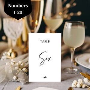 Może przedstawiać: Biała karta z numerem stołu z czarnym tekstem, który brzmi "TABLE Six" i inicjałami "S♥J".