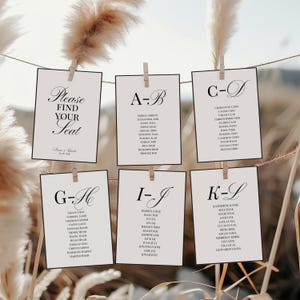May include: A wedding seating plan with names arranged alphabetically. Cream-coloured cards are suspended by pegs on a string. The top card says "Please Find Your Seat". The background includes dried ornamental grass.