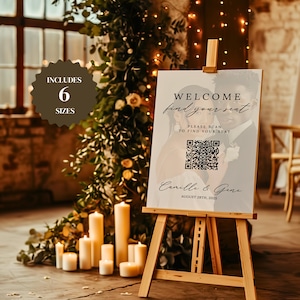 以下が含まれることがあります： 木製のイーゼルには、「WELCOME find your seat」と書かれたウェルカムボードが飾られています。ボードにはQRコードと「Camille & Gene」の名前、2025年8月28日の日付が含まれています。画像には、キャンドルと緑も写っています。