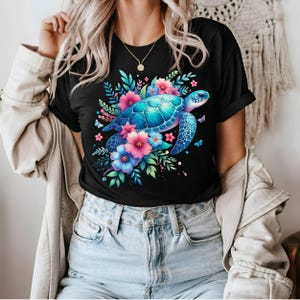 以下が含まれることがあります： 黒いTシャツ。鮮やかなウミガメのイラストが描かれており、カラフルな花と蝶が周りに描かれています。カメは青とターコイズ色の甲羅で、ピンクと青の花があります。デザインは詳細で目を引きます。