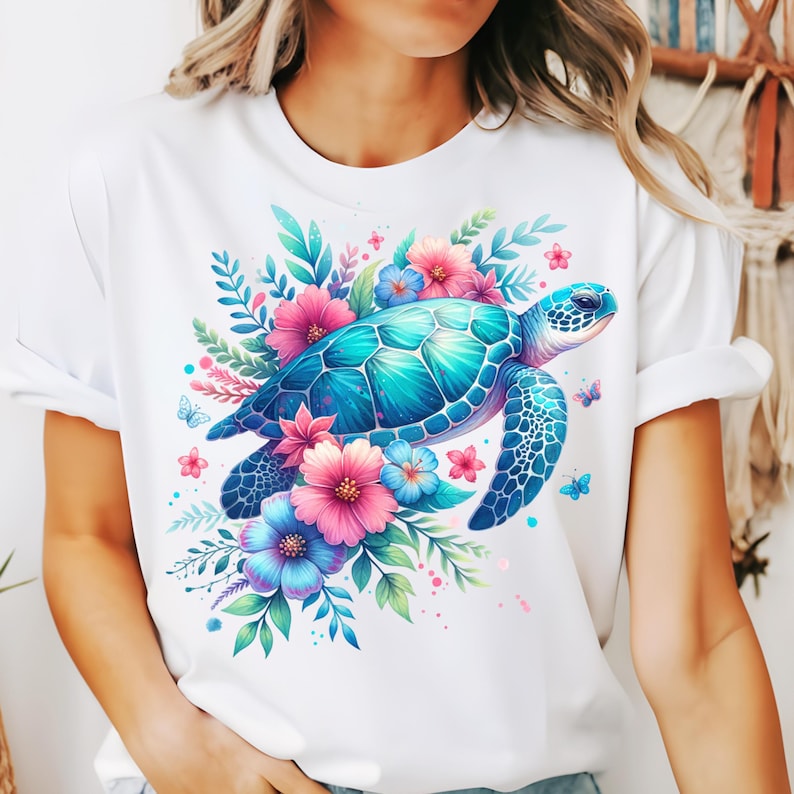 以下が含まれることがあります： 鮮やかなウミガメのイラストが描かれた白いTシャツ。カメは青とターコイズの色合いで描かれ、ピンクと青の花、緑の葉、小さな蝶に囲まれています。デザインは詳細でカラフルです。