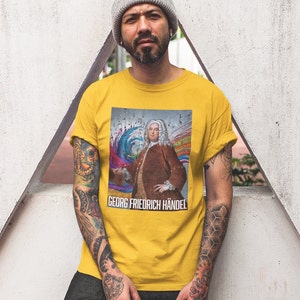 May include: A yellow t-shirt with a colorful graphic of Georg Friedrich Händel, a famous composer, surrounded by musical notes. The text "GEORG FRIEDRICH HÄNDEL" is printed below the graphic.