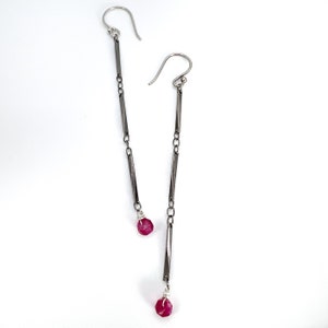 May include: A pair of long silver earrings with a chain link design and a pink gemstone dangling at the bottom of each earring.