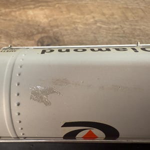 K&ouml;nnte beinhalten: Nahaufnahme eines silbernen Tankwagens mit dem Wort "Diamond" in Schwarz aufgedruckt. Der Tankwagen hat ein schwarz-oranges Logo und die Worte "Safety Valves" sind sichtbar. Der Tankwagen hat Nieten und einige Abnutzungserscheinungen.