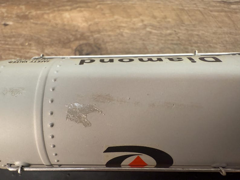 K&ouml;nnte beinhalten: Nahaufnahme eines silbernen Tankwagens mit dem Wort "Diamond" in Schwarz aufgedruckt. Der Tankwagen hat ein schwarz-oranges Logo und die Worte "Safety Valves" sind sichtbar. Der Tankwagen hat Nieten und einige Abnutzungserscheinungen.