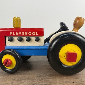 May include: A vintage Playskool wooden toy tractor. The tractor is painted red, blue, white, and yellow, with black wheels. The word "PLAYSKOOL" is printed on the red body. A wooden figure is seated in the driver's seat.