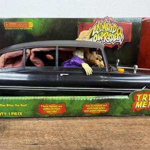 May include: Animated lowrider toy car in a box. The black car has a figure in the driver's seat wearing a purple shirt. The box has text that says "Animated Low Rider" and "Try Me!"