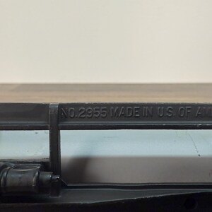 K&ouml;nnte beinhalten: Nahaufnahme eines schwarzen Metallobjekts mit dem gepr&auml;gten Text "NO.2955 MADE IN U.S. OF AMERICA". Das Objekt scheint Teil eines gr&ouml;&szlig;eren Mechanismus oder Werkzeugs zu sein.