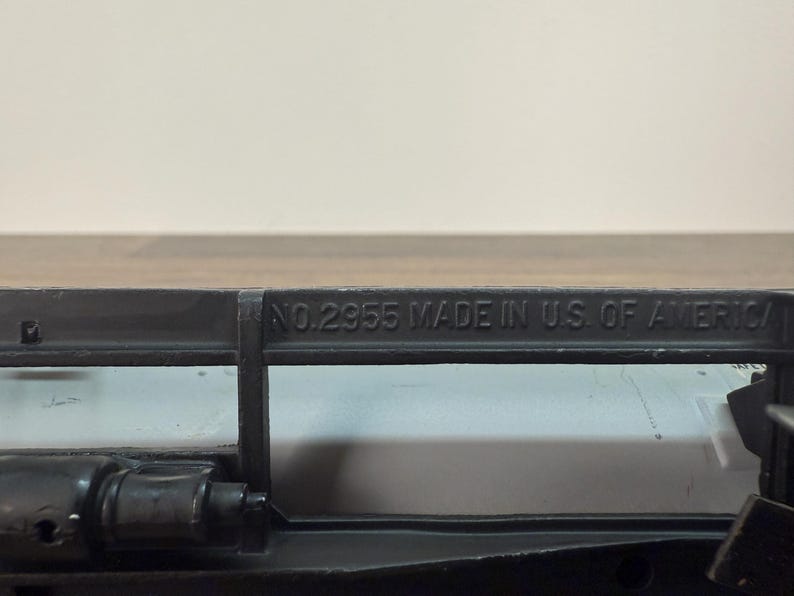 K&ouml;nnte beinhalten: Nahaufnahme eines schwarzen Metallobjekts mit dem gepr&auml;gten Text "NO.2955 MADE IN U.S. OF AMERICA". Das Objekt scheint Teil eines gr&ouml;&szlig;eren Mechanismus oder Werkzeugs zu sein.