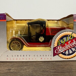 May include: A die-cast metal 1916 Studebaker Liberty Classic bank model in its original box. The model car is red and black with gold-colored wheels. The box features the Studebaker logo and the text "Die-Cast Metal".
