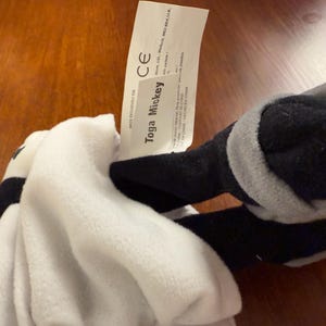 May include: White and grey plush toy with black accents. The toy is labelled "Toga Mickey" with a CE mark.