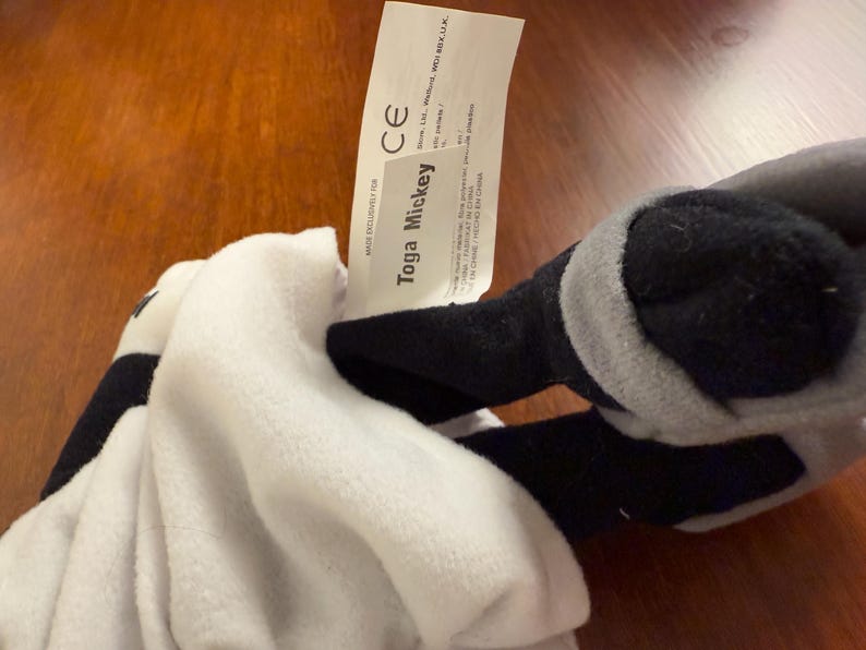 May include: White and grey plush toy with black accents. The toy is labelled "Toga Mickey" with a CE mark.