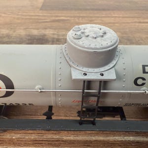 K&ouml;nnte beinhalten: Ein hellgrauer Modellzugwagen mit zylindrischem Oberteil und kleiner Leiter. Der Wagen tr&auml;gt den Text "Dia Chem" und ein Logo mit einem roten Dreieck. Das Modell steht auf einer Holzoberfl&auml;che.
