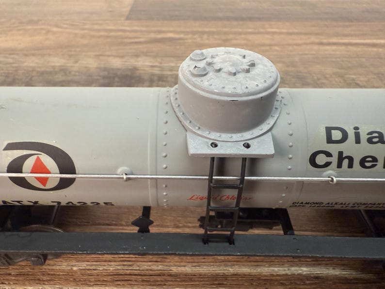 K&ouml;nnte beinhalten: Ein hellgrauer Modellzugwagen mit zylindrischem Oberteil und kleiner Leiter. Der Wagen tr&auml;gt den Text "Dia Chem" und ein Logo mit einem roten Dreieck. Das Modell steht auf einer Holzoberfl&auml;che.