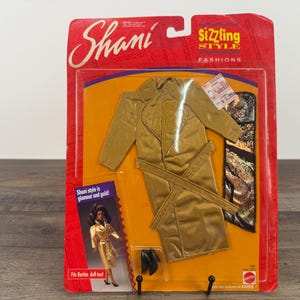May include: A gold-colored Shani doll fashion set, still in its original packaging. The set includes a long coat with a belt and black shoes. The packaging is red with the words "Sizzling Style Fashions" and "Shani" printed on it.