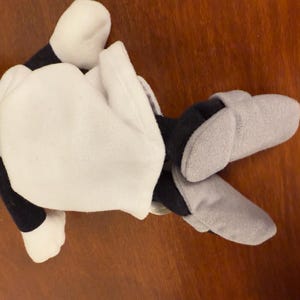 May include: A plush toy with a white body, black arms and legs, and a green head. The toy is wearing grey slippers.
