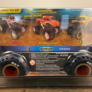 May include: A boxed set of three True Metal monster trucks, including "Zombie", "El Toro Loco", and "Earth Shaker". The packaging reads "Collect 'Em All!" and "1/24 Scale". The tires are black with red accents.