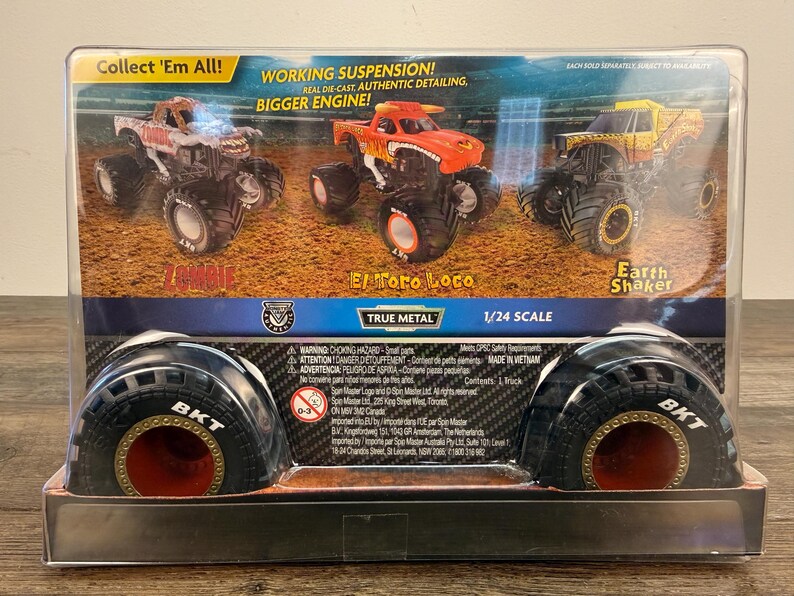 May include: A boxed set of three True Metal monster trucks, including "Zombie", "El Toro Loco", and "Earth Shaker". The packaging reads "Collect 'Em All!" and "1/24 Scale". The tires are black with red accents.