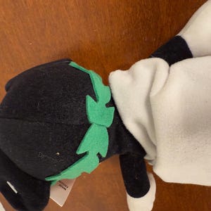 May include: Black and white plush toy with a green felt hat and a white felt body. The toy has a tag that says "Made in Korea".
