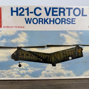 May include: Hobby Craft H21-C Vertol Workhorse model kit box. The box features a painted image of a military helicopter against a cloudy sky. The box has the text "H21-C Vertol Workhorse" in blue.
