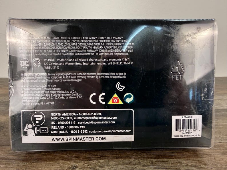 May include: A black box with text and logos, including "Wonder Woman" and "DC Comics." The box has a barcode and contact information for Spin Master. The box is made of a clear plastic.