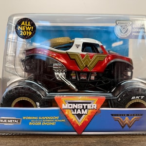 May include: A red, white, and gold Wonder Woman Monster Jam truck toy in a clear plastic package. The toy truck has large black tyres and the Wonder Woman logo. The package includes the text "ALL NEW! 2019" and "MONSTER JAM".