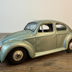 May include: A vintage, light green toy car with black tires and silver accents. The classic car has a rounded body, curved fenders, and a detailed front end. The toy car is a collectible item.