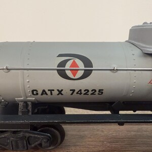 K&ouml;nnte beinhalten: Ein grauer Modell-Eisenbahn-Tankwagen mit dem Text "GATX 74225" und einem schwarz-roten Logo. Der Tankwagen hat eine Leiter und die Worte "Liqu Chlor" in Rot. Der Wagen steht auf einer schwarzen Schiene.