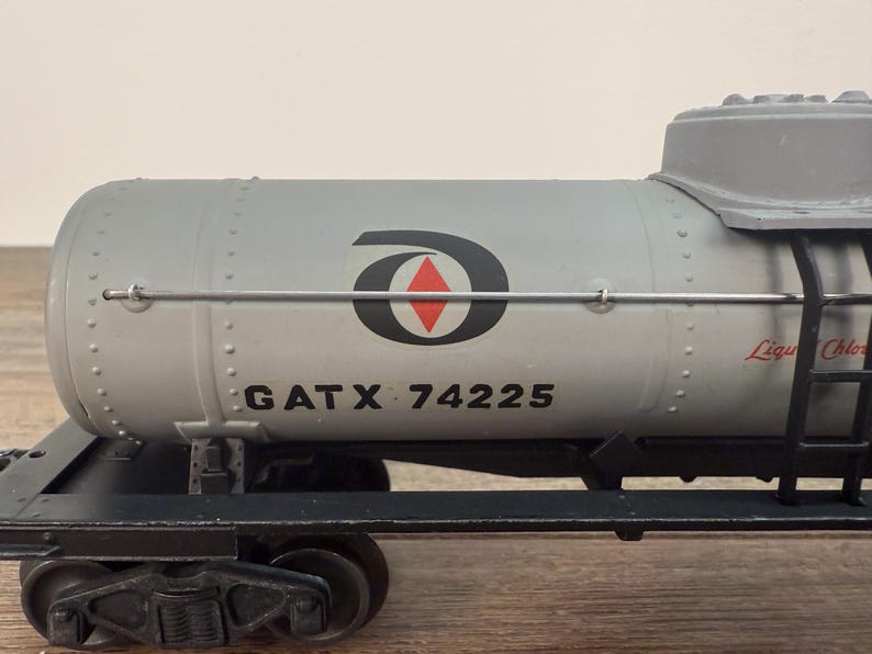 K&ouml;nnte beinhalten: Ein grauer Modell-Eisenbahn-Tankwagen mit dem Text "GATX 74225" und einem schwarz-roten Logo. Der Tankwagen hat eine Leiter und die Worte "Liqu Chlor" in Rot. Der Wagen steht auf einer schwarzen Schiene.