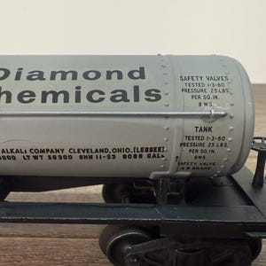 K&ouml;nnte beinhalten: Graues Diamond Chemicals Tankwagenmodell mit schwarzen R&auml;dern und Fahrgestell. Der Tankwagen tr&auml;gt die Aufschrift "Diamond Chemicals" und Details zur Kapazit&auml;t und Sicherheit des Tanks.