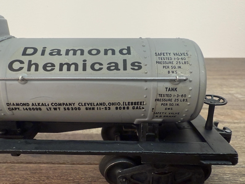 K&ouml;nnte beinhalten: Graues Diamond Chemicals Tankwagenmodell mit schwarzen R&auml;dern und Fahrgestell. Der Tankwagen tr&auml;gt die Aufschrift "Diamond Chemicals" und Details zur Kapazit&auml;t und Sicherheit des Tanks.