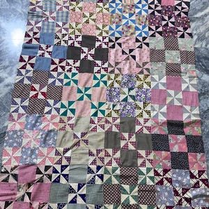 May include: A vintage quilt made of patchwork squares with a windmill design. The quilt is made of various fabrics in shades of pink, blue, green, white, and brown.