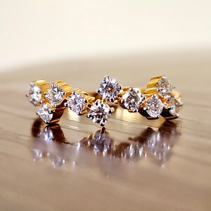 May include: A gold band ring with a cluster of small, clear diamonds set in a wave-like pattern.