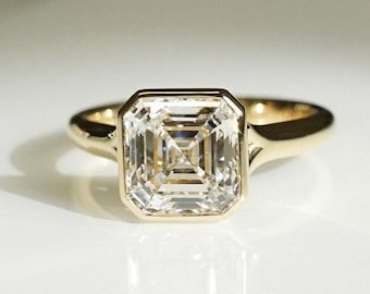 Puede incluir: Un anillo de oro con una piedra preciosa cuadrada, transparente y facetada, engastada en un engaste de bisel.