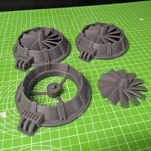 May include: Three grey plastic fan models, one with a removable fan blade. The fan models have a circular base with a raised rim and a central hub with spokes. The fan blades are designed with a central hub and multiple blades.