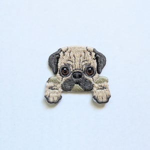 Könnte beinhalten: Gestickter Bügelaufkleber mit einem braunen und weißen Mops, der hinter einem grün-weiß gestreiften Objekt hervorlugt.