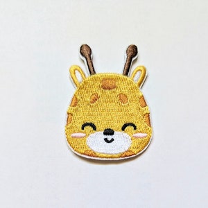 May include: An embroidered patch featuring a cartoon giraffe with brown antlers, a white face, and a smiling expression.