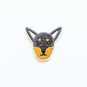 May include: Embroidered iron-on patch of a black and tan dog's head with yellow eyes.